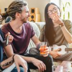 Young female smoking joint with cannabis while playing on music instruments at home with friends
